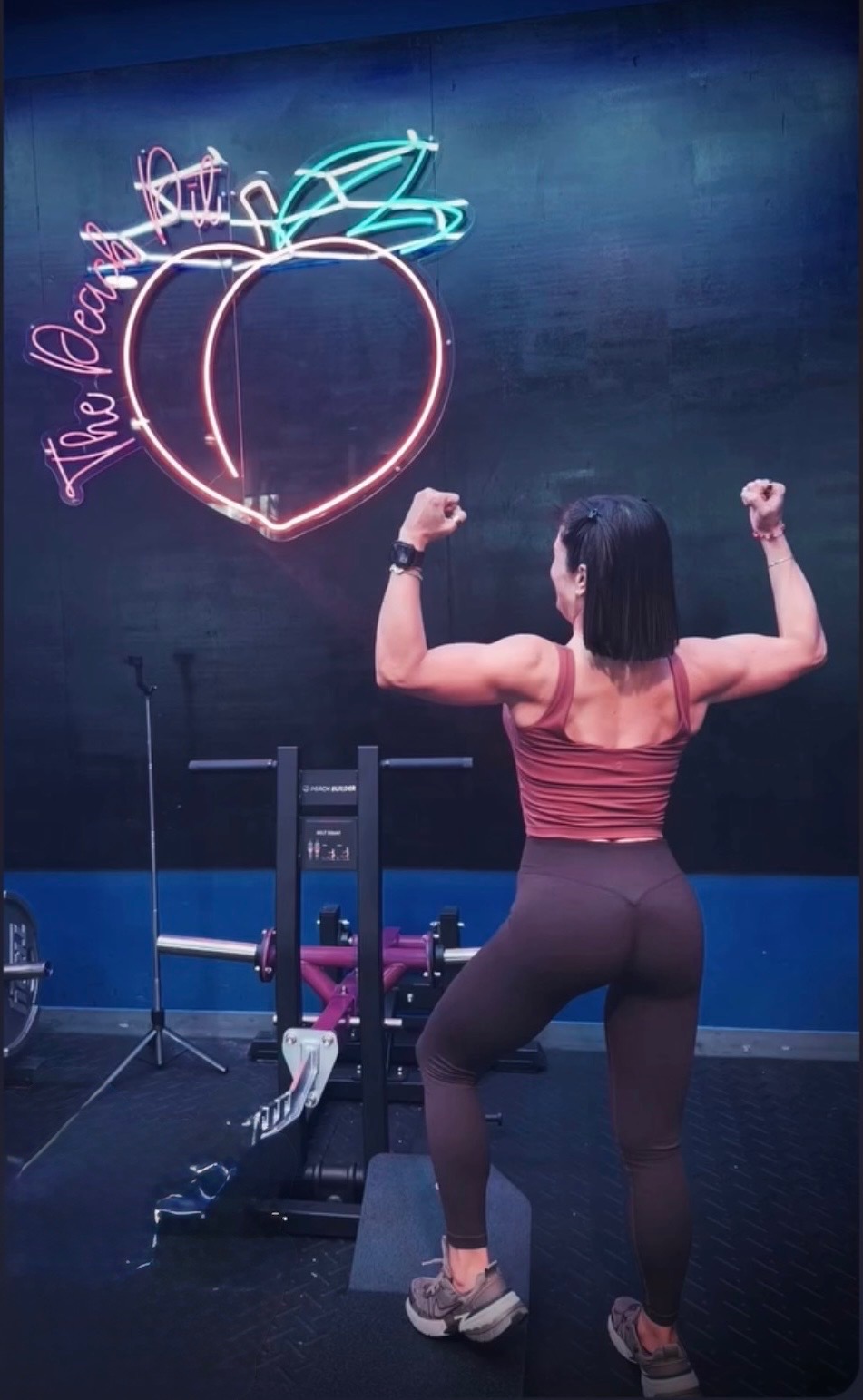 P-FIT North Cape client flexing in front of the neon Peach Pit sign